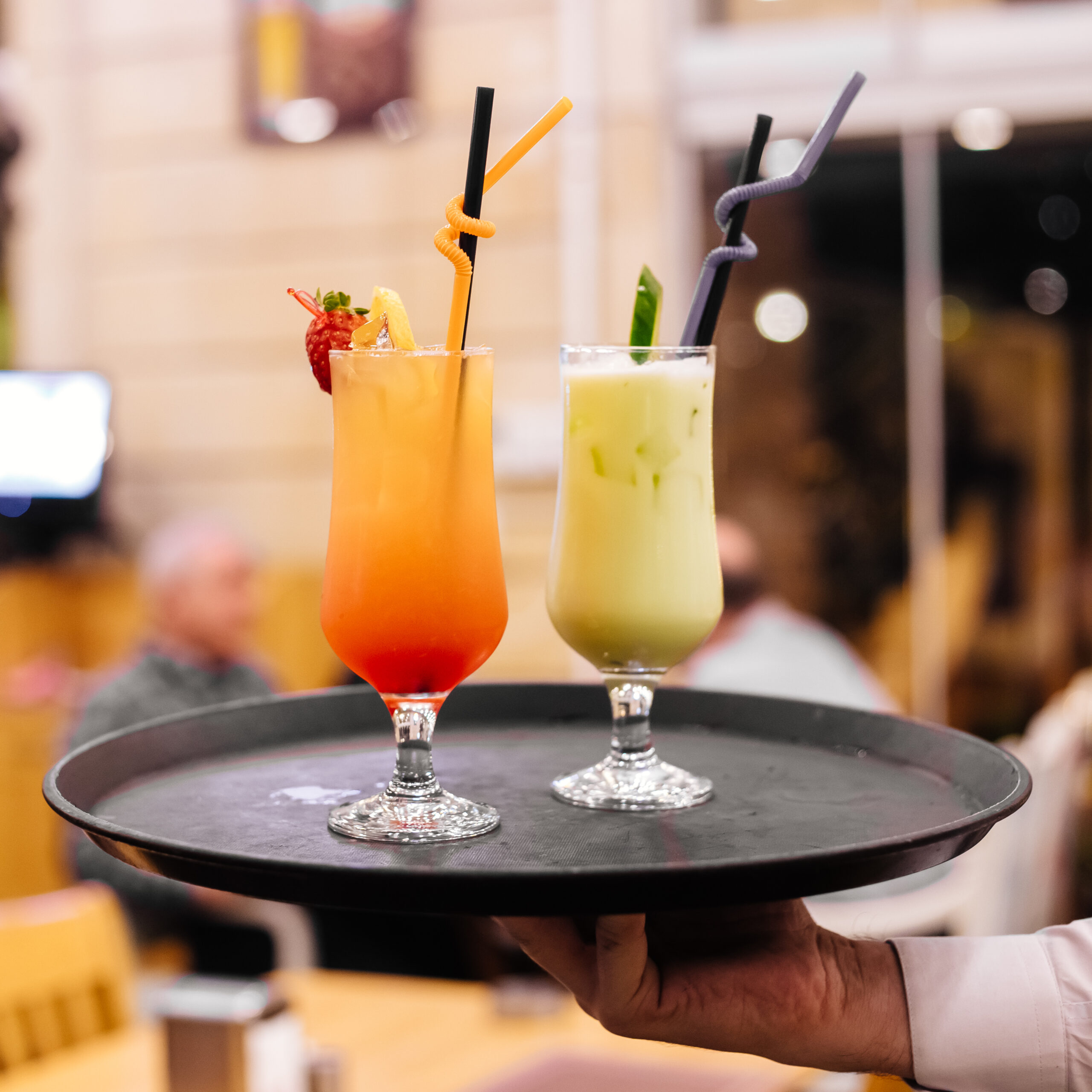 front view a man holds a tray with two cocktails