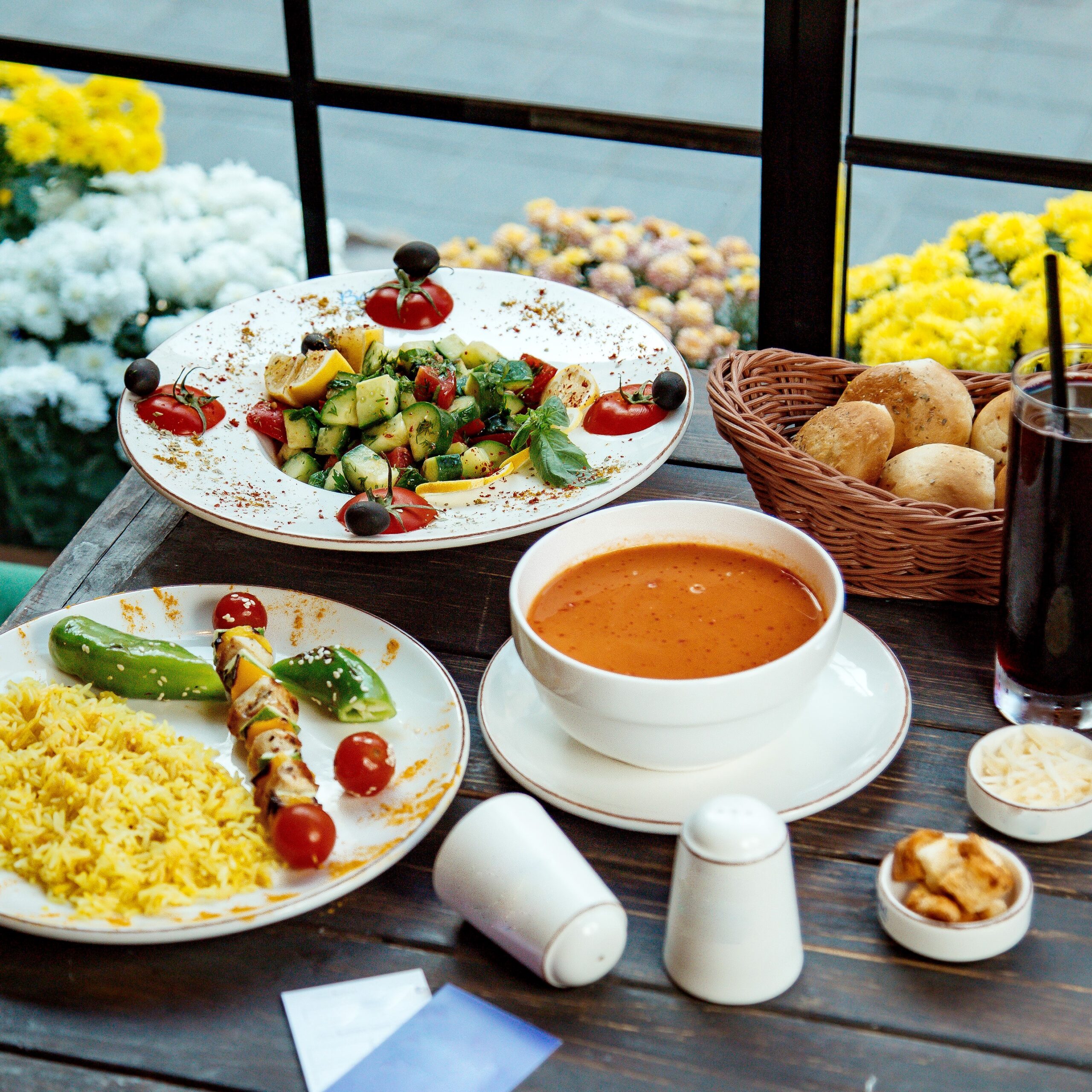 a lunch setup with rice and chicken skewers greek salad and lentil soup